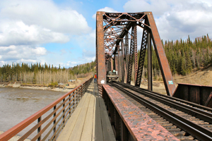 A crew member watches as wind turbine generators parts are hauled across a bridge over the Nenana River to the project site.